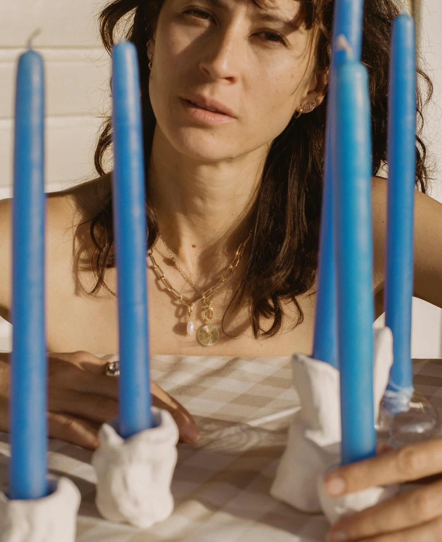Woman wearing golden necklaces behind blue candles