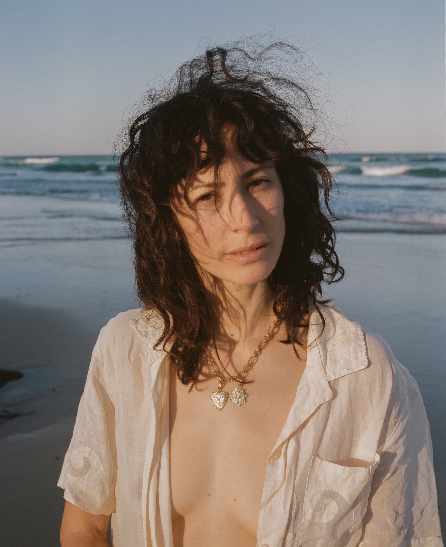 Woman at the beach with white open shirt and gold necklace